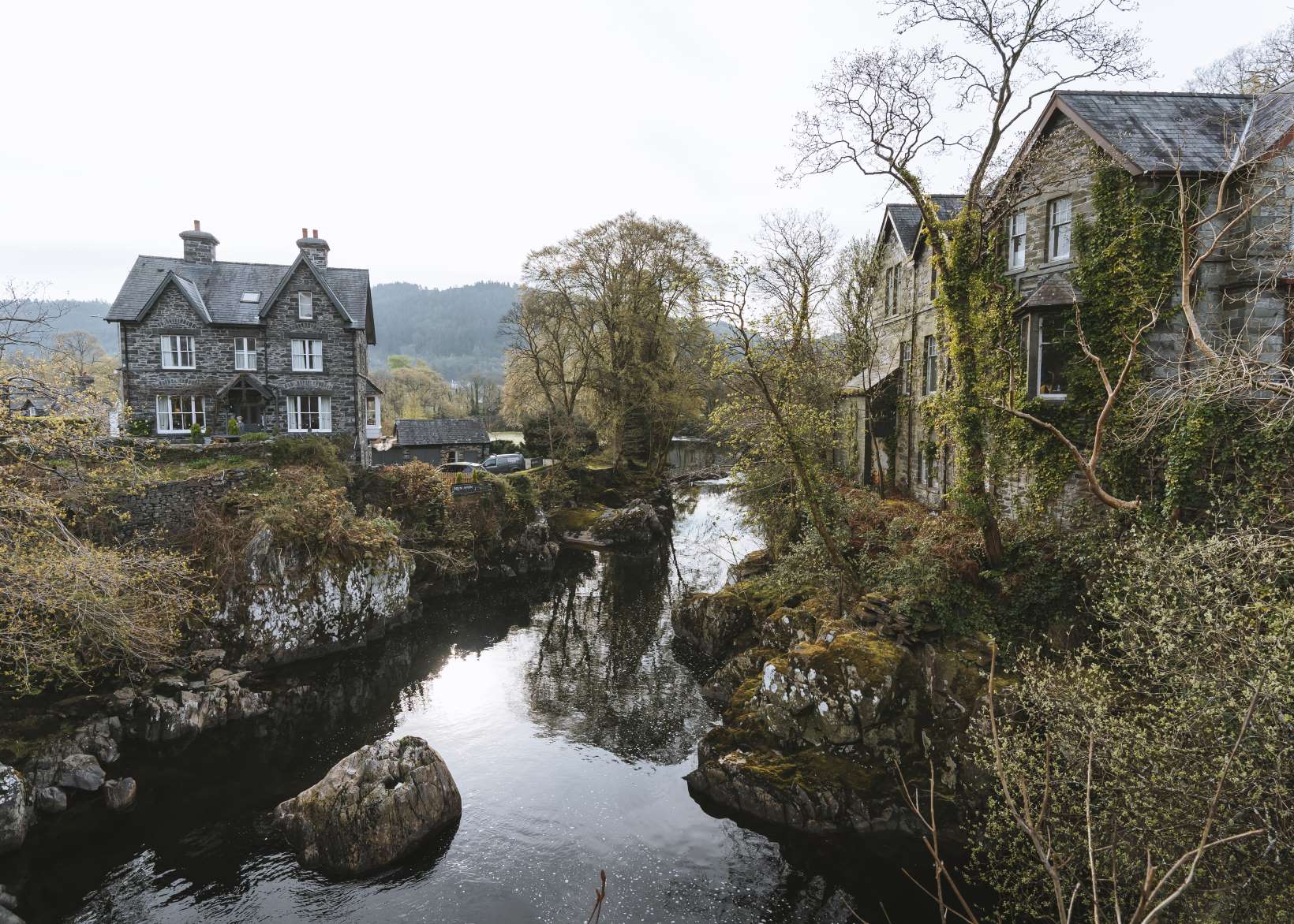The Llugwy river runs through the village of Betws y Coed with stone houses on either side.